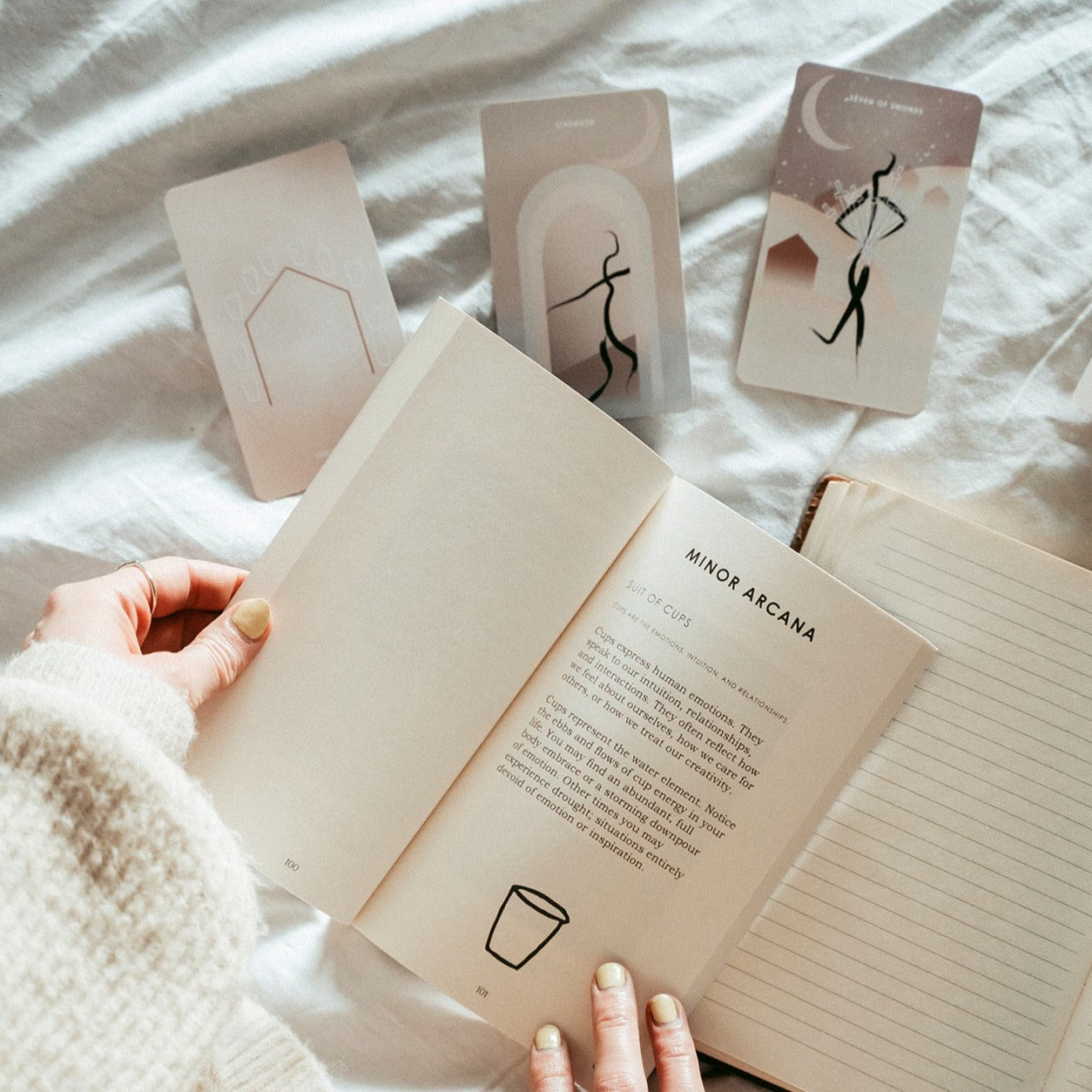 hands opening a tarot guidebook with a tarot reading in front